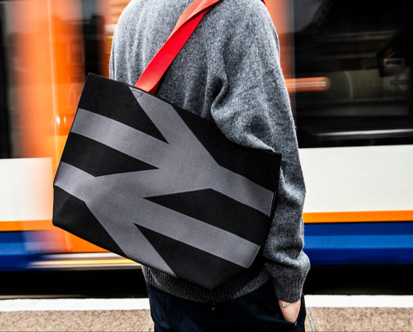 Person holding a black bag with geometric design in front of a blurred train