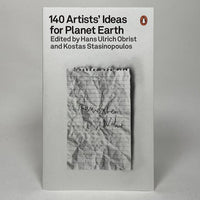 The cover of a book titled "140 Artists' Ideas for Planet Earth," with a minimalist design, featuring a monochrome photograph of a crumpled piece of paper with handwritten notes.