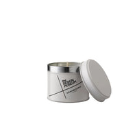 A minimalist white wax candle in a silver metal tin with its lid leaning against the side, featuring black text that reads 'the DESIGN MUSEUM' and 'CRANBOURN LONDON' on a clean white background.