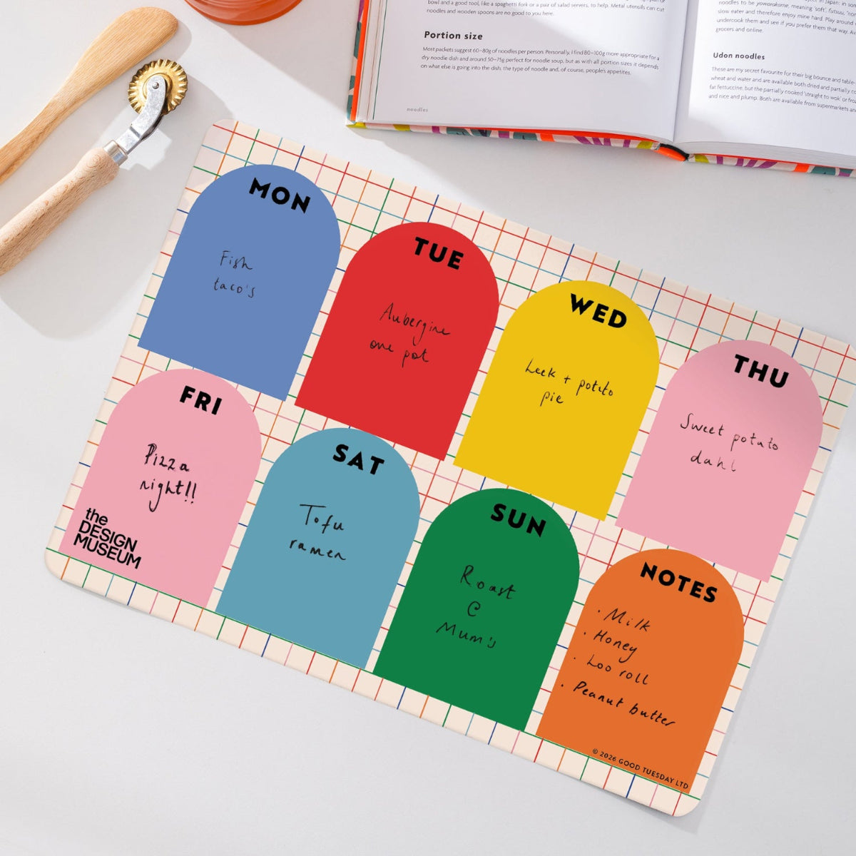 A weekly planner notepad with eight colorful arch-shaped daily sheets laid out on a white surface. The notepad has a white grid background with thin red and green lines, and the daily pages are blue, red, yellow, pink, teal, light blue, green, and orange.