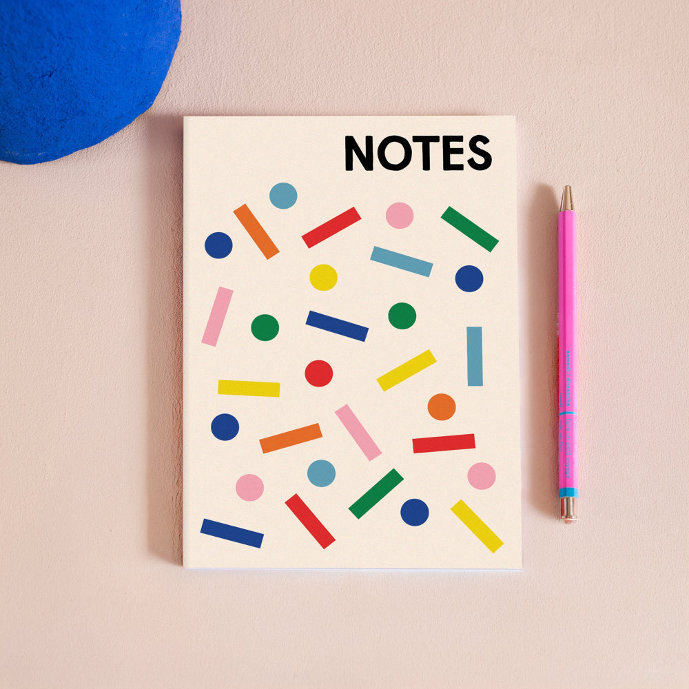 Colourful notebook with a pink pen next to it on a pink background