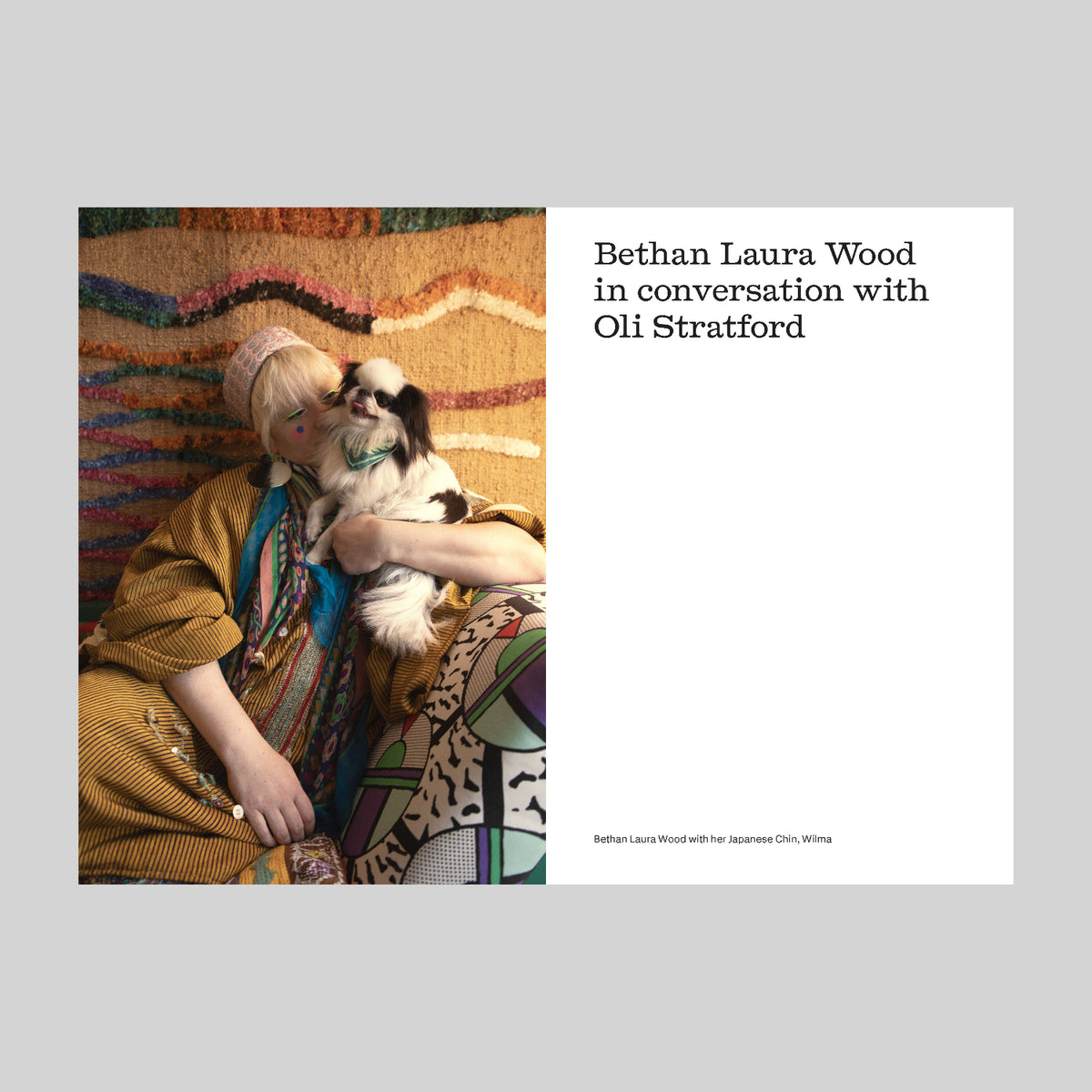 A book page showing a person holding a dog on a colorful rug on a grey background.