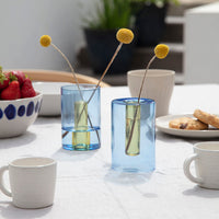 Two small blue and yellow reversibe vases with flowers inside on a table.