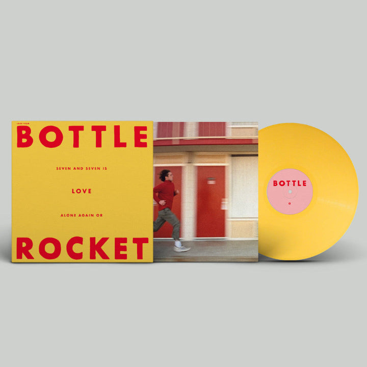 Vinyl record album packaging and disc shown on a light gray background. The square cover features a yellow field with large red text reading 'BOTTLE ROCKET' and a photo of a person walking in front of a red door.