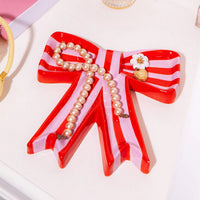 A red and pink striped bow shaped trinket tray with pieces of jewellery in it.