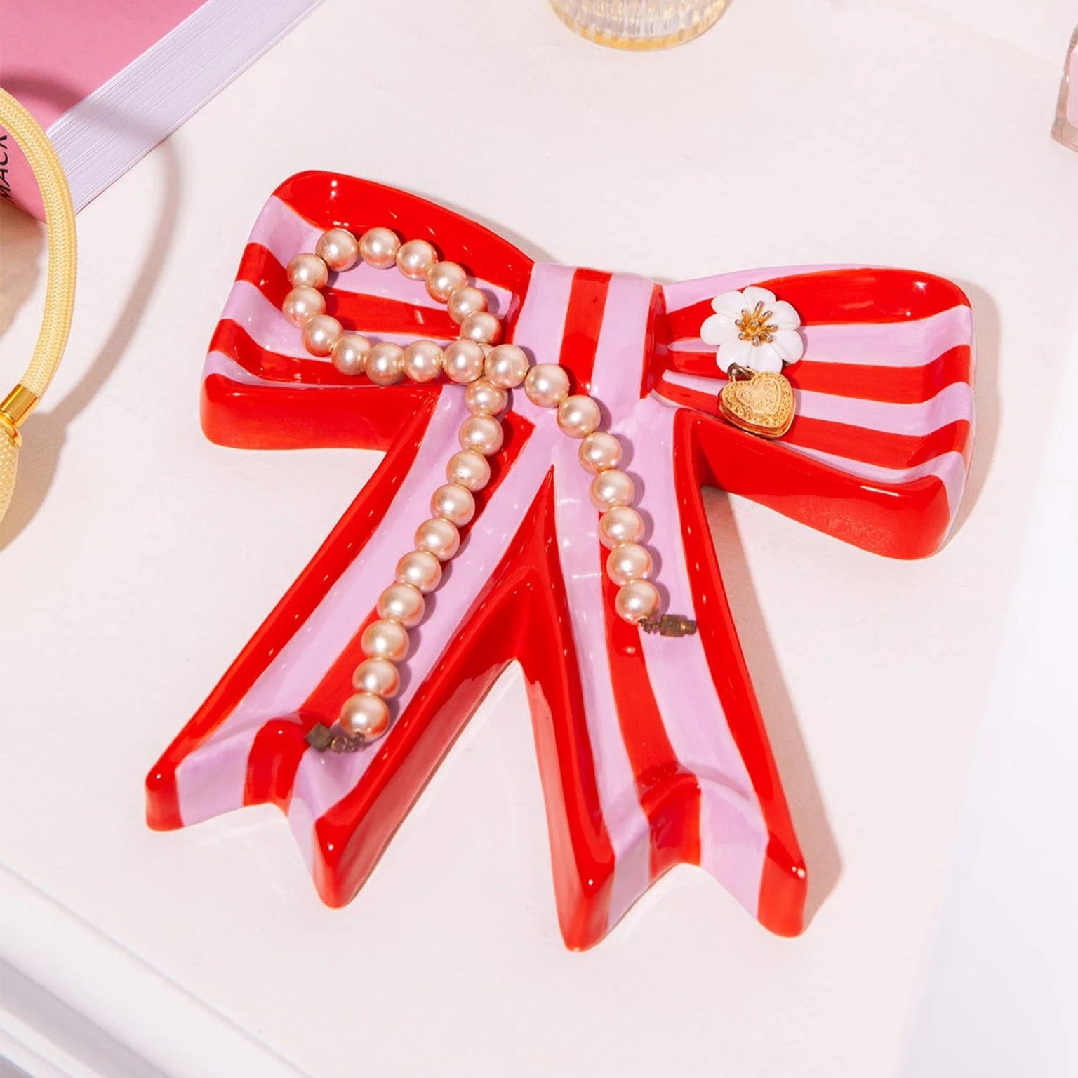 A red and pink striped bow shaped trinket tray with pieces of jewellery in it.