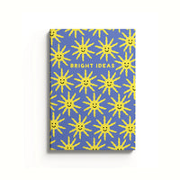 A notebook with a blue cover featuring a pattern of yellow sun shapes and the text 'BRIGHT IDEAS' on the front.