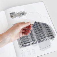 The inside of Brutal Britain paper model book featuring a hand pulling out a paper cut-out of a Brutalist building part.