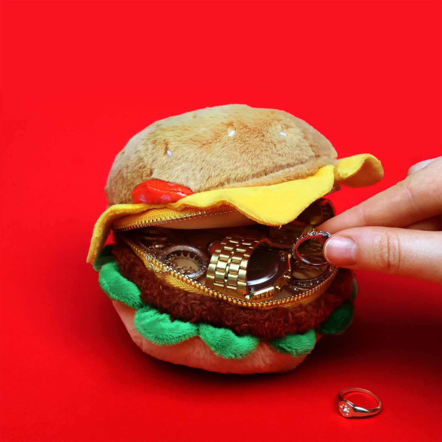 Hamburger-shaped coin purse with a hand interacting on a red background