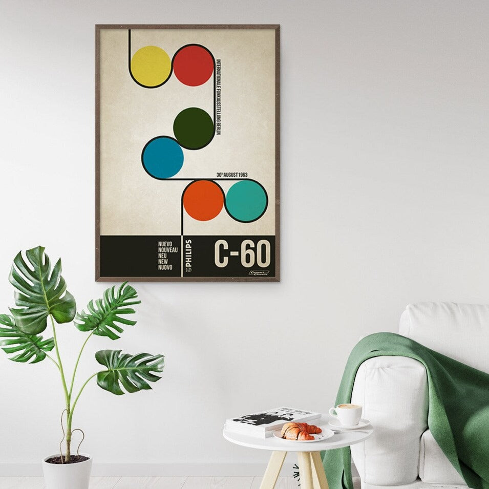 A vintage style poster featuring colorful circles and the text 'C-60' related to the 1963 Berlin Radio Show advertisement for a cassette player displayed on a wall next to a plant and a sofa.