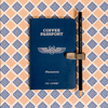 Blue 'Coffee Passport' book with a pen on a patterned background