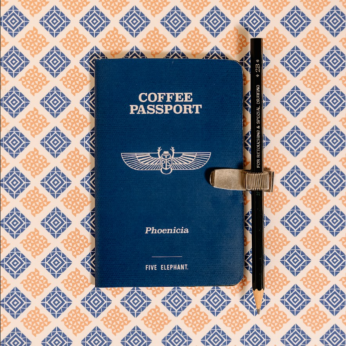 Blue 'Coffee Passport' book with a pen on a patterned background