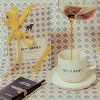 Hand pouring coffee into a 'Five Elephant' mug with a gift box and notebook in the background.