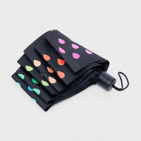 A closed colour changing umbrella with a colourful raindrop pattern on a black background.