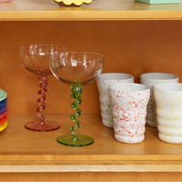Wooden shelf with colorful vases, plates, and glasses against a white wall.
