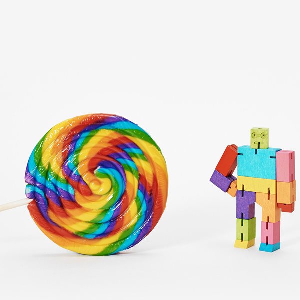 A colorful cubebot toy in a pose resembling a person next to a multicolored spiral lollipop.
