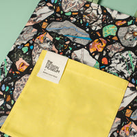 Two tote bags with a colorful abstract pattern on one and a solid yellow color on the other, against a light green background.