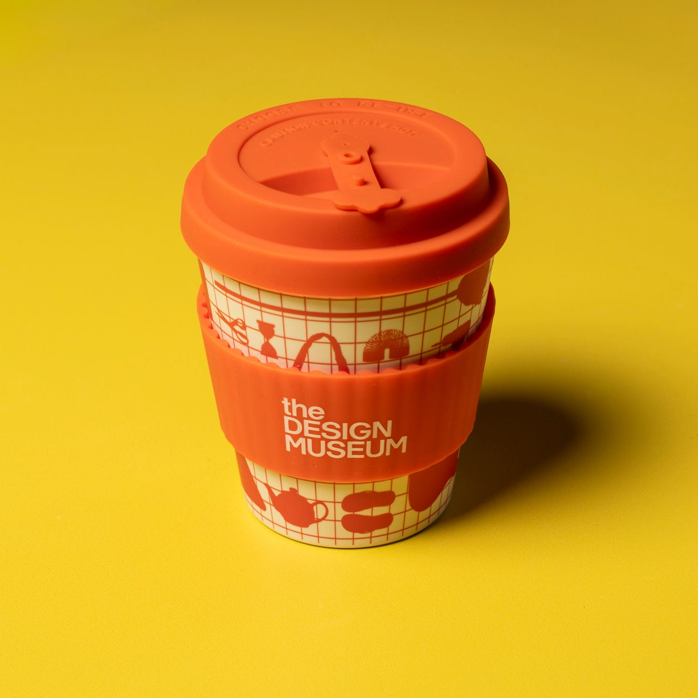 Red coffee cup with a lid on a yellow background, featuring 'The Design Museum' branding.