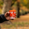 Person holding a red coffee cup with a blurred outdoor background