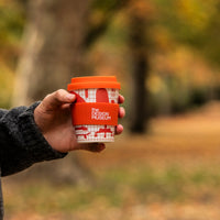 Person holding a red coffee cup with a blurred outdoor background