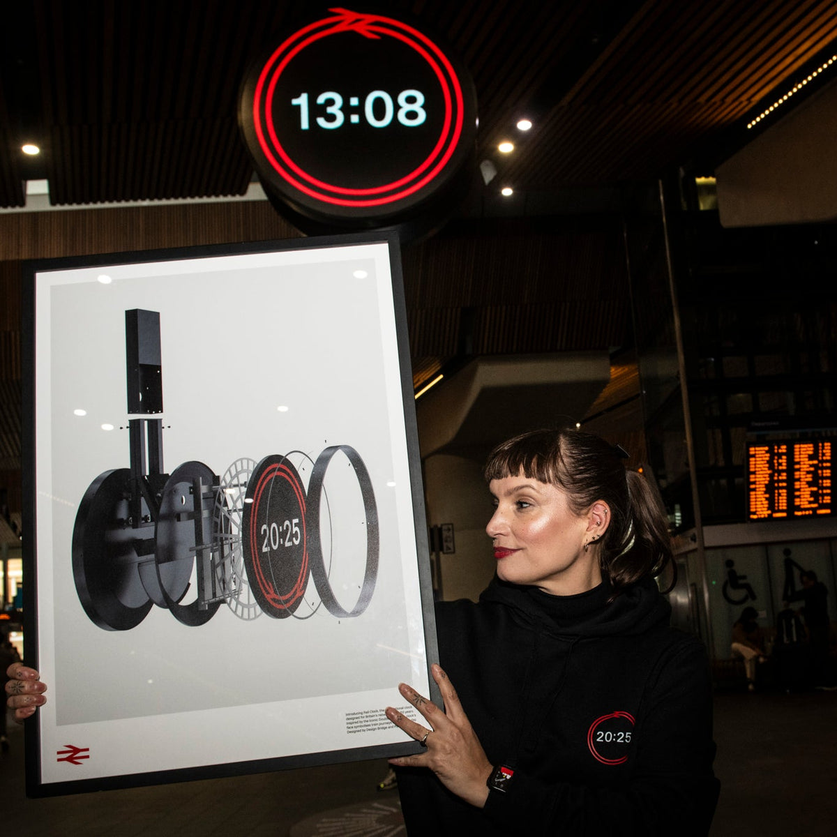 Person holding a large framed picture of Adidas products in an indoor setting with a clock displaying 13:08.