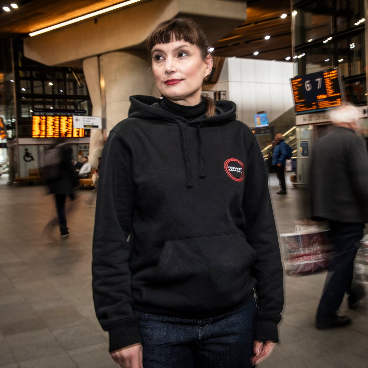 Person wearing a black hoodie with a logo in a busy indoor setting