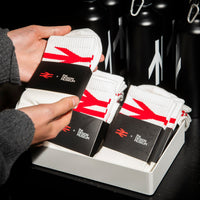 Person holding a pair of white socks with red and black branding on a dark background