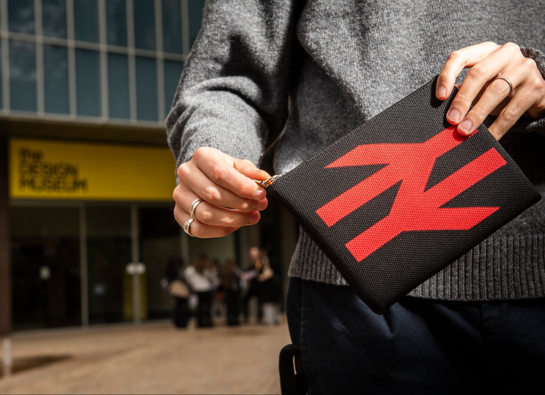 Person holding a black pouch with a red logo in front of The Design Museum.