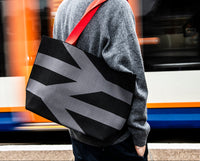 Person holding a black bag with geometric design in front of a blurred train
