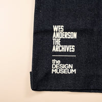 Black fabric with white text 'Wes Anderson The Archives' and 'The Design Museum' on a beige background