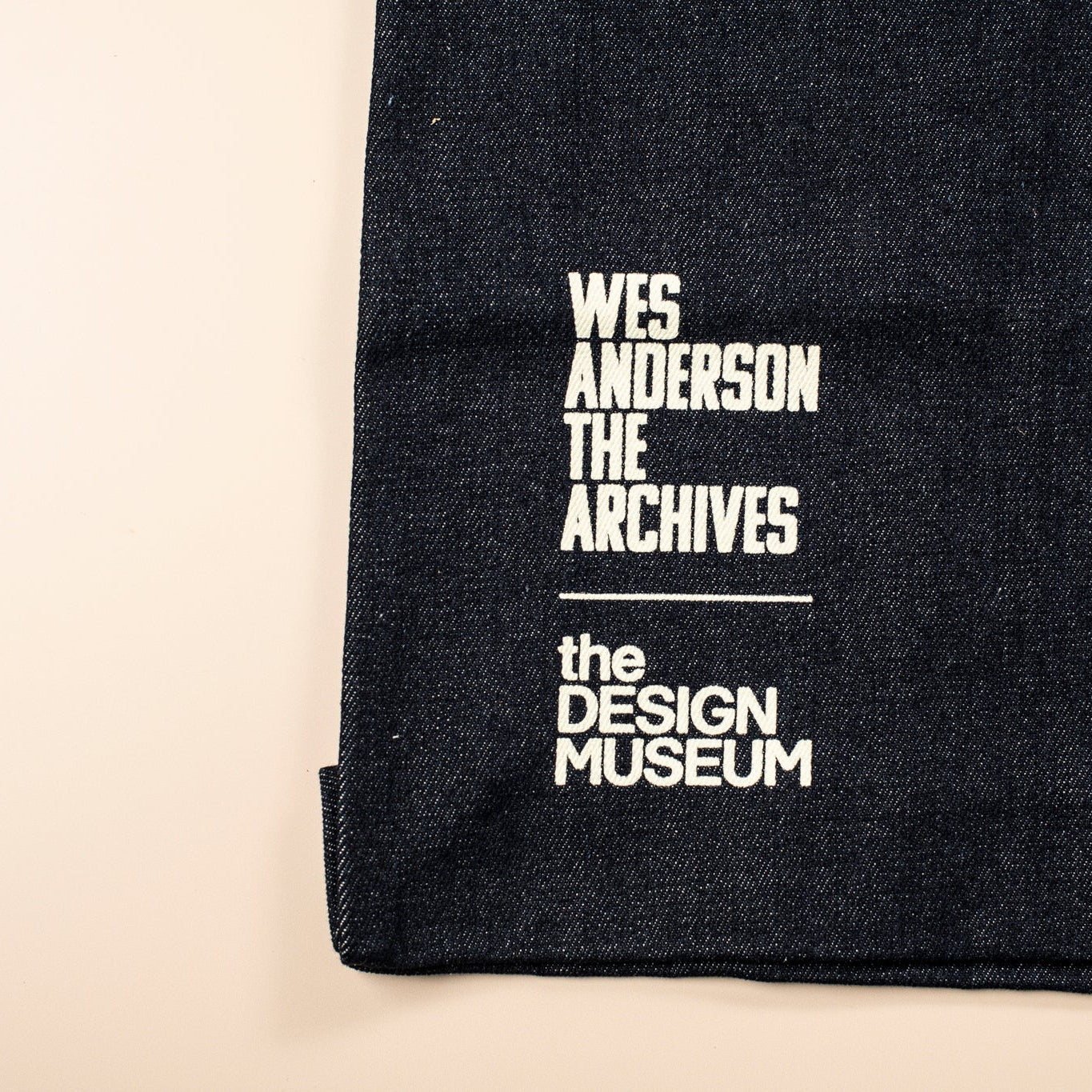 Black fabric with white text 'Wes Anderson The Archives' and 'The Design Museum' on a beige background