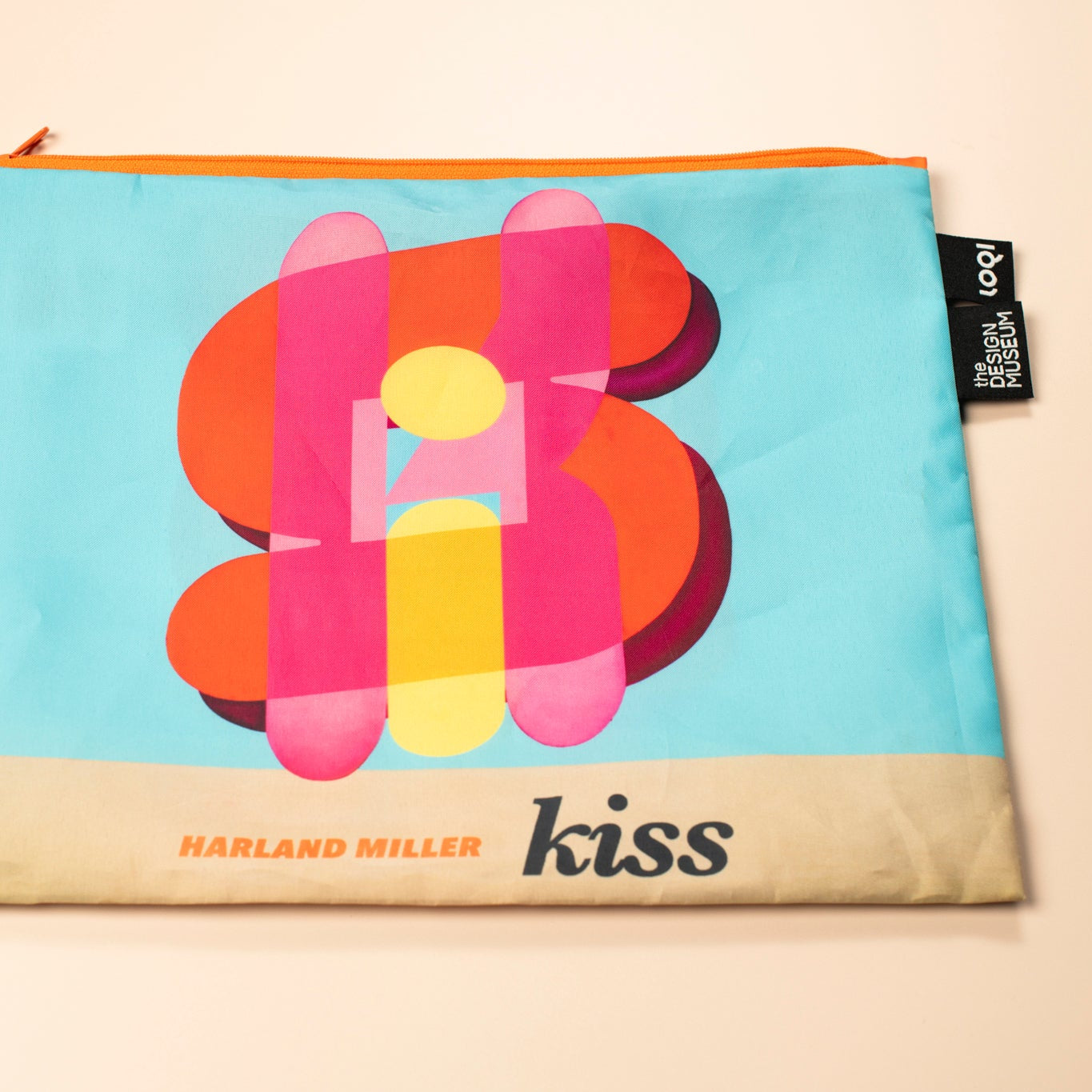 Colorful pouch with 'kiss' design and Harland Miller branding on a beige background