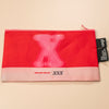 Red pouch with pink 'X' design and visible brand tag on a beige background