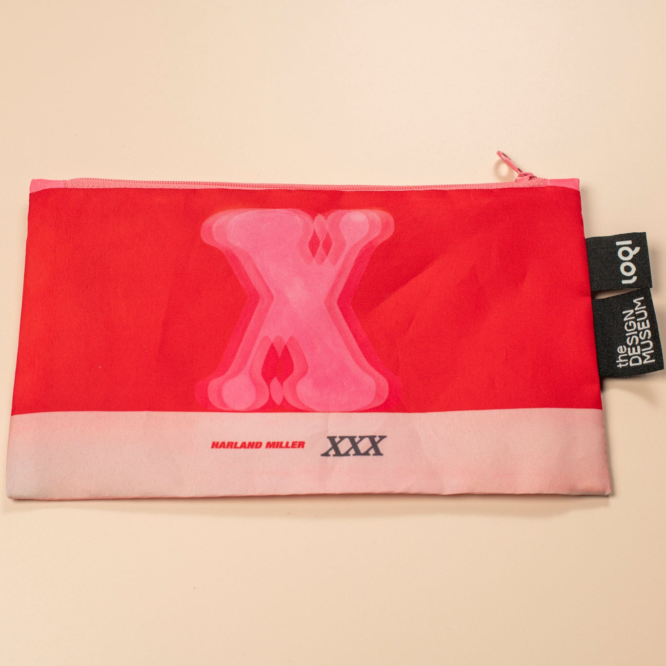 Red pouch with pink 'X' design and visible brand tag on a beige background