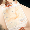 Map titled 'The Phoenician Scheme' held by a person on a light surface.