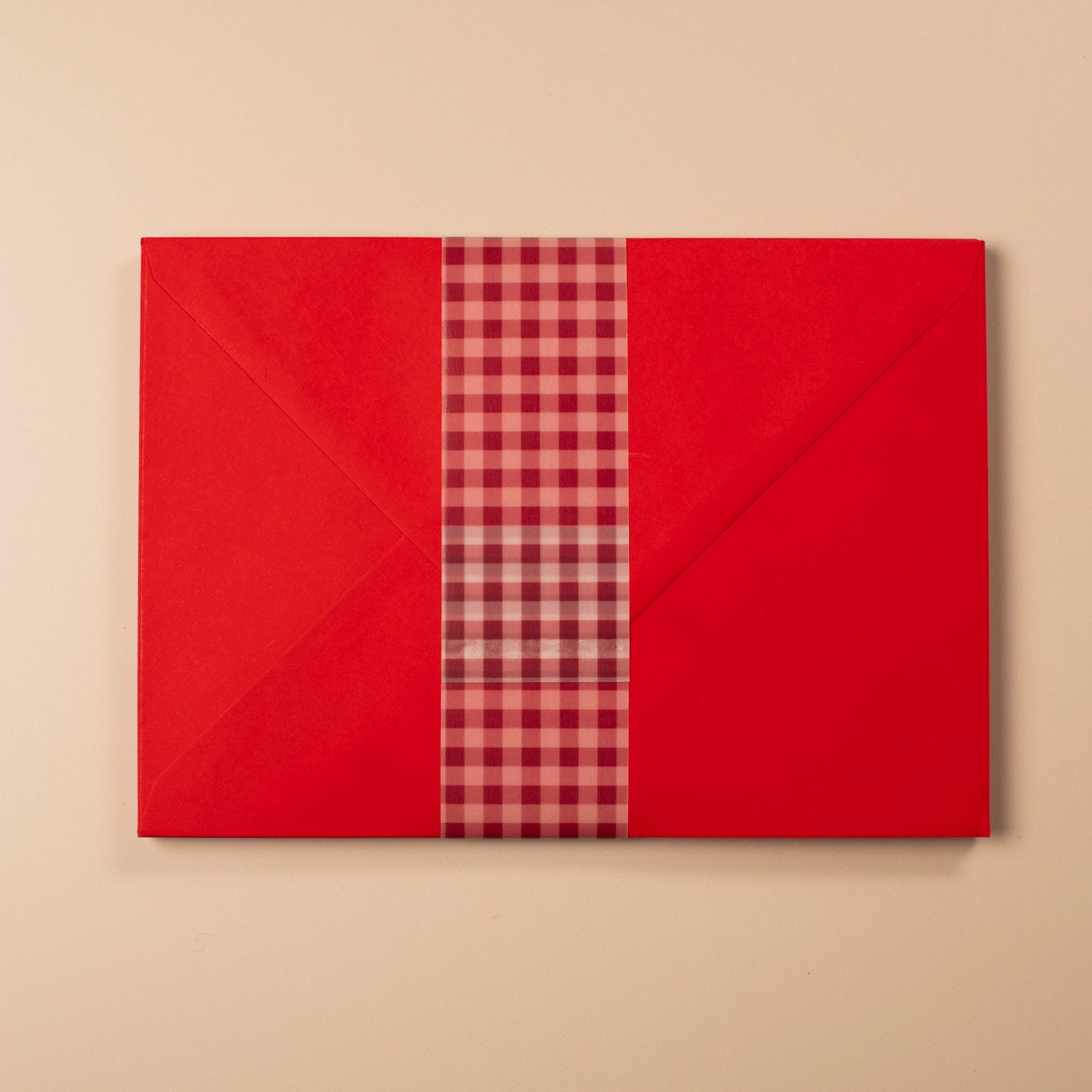 Red gift box with a plaid ribbon on a beige background
