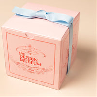 Pink gift box with a blue ribbon from the Design Museum on a beige background