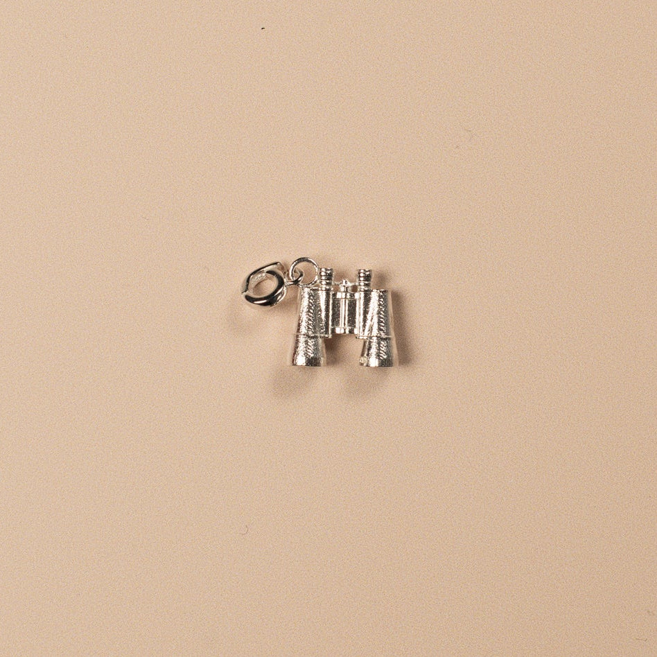 Silver binocular charm on a beige background