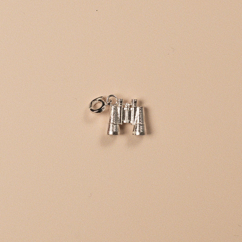 Silver binocular charm on a beige background
