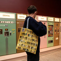 Person with a patterned bag standing in front of vintage vending machines.