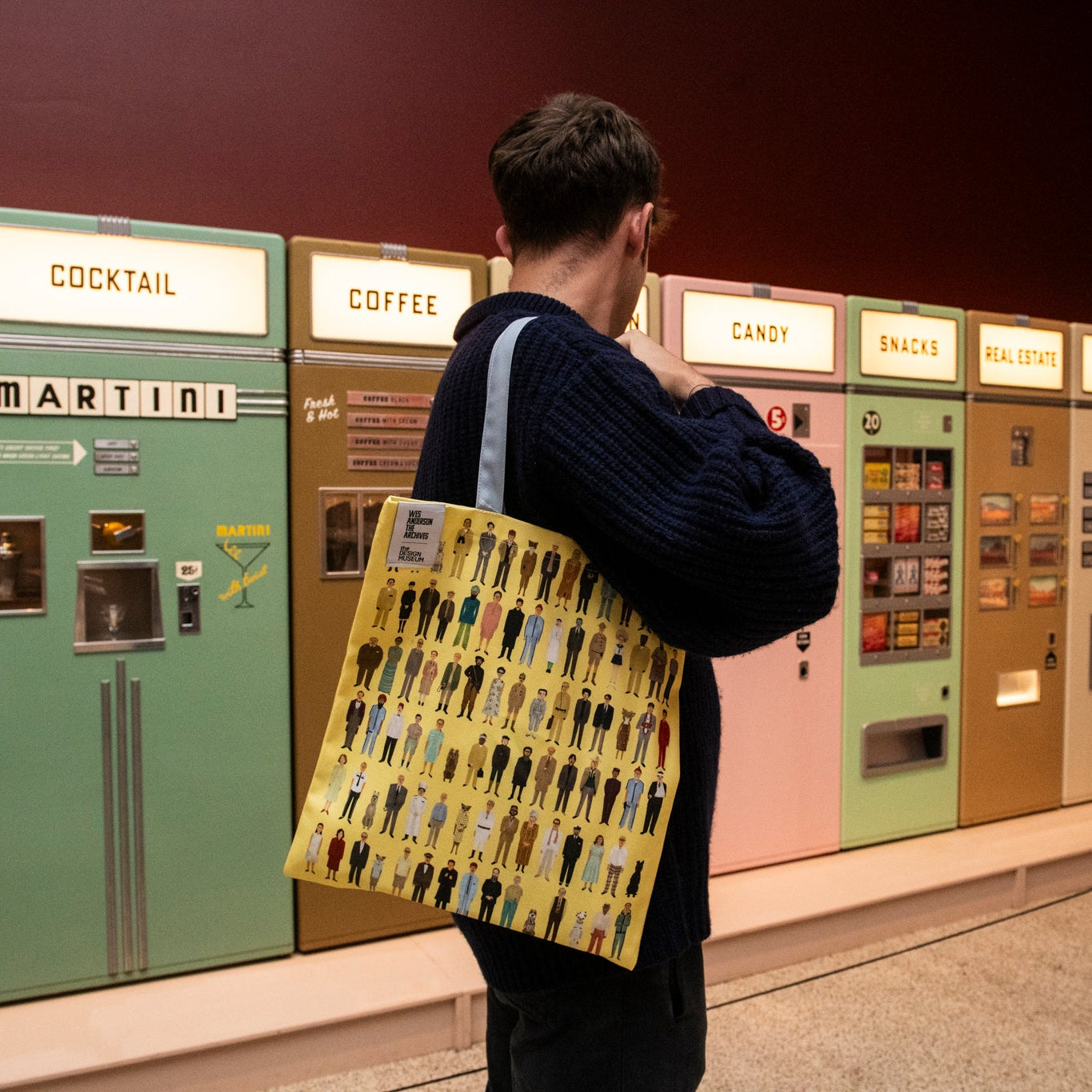 Person with a patterned bag standing in front of vintage vending machines.