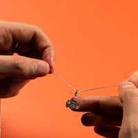 Person holding a necklace with a pendant against an orange background