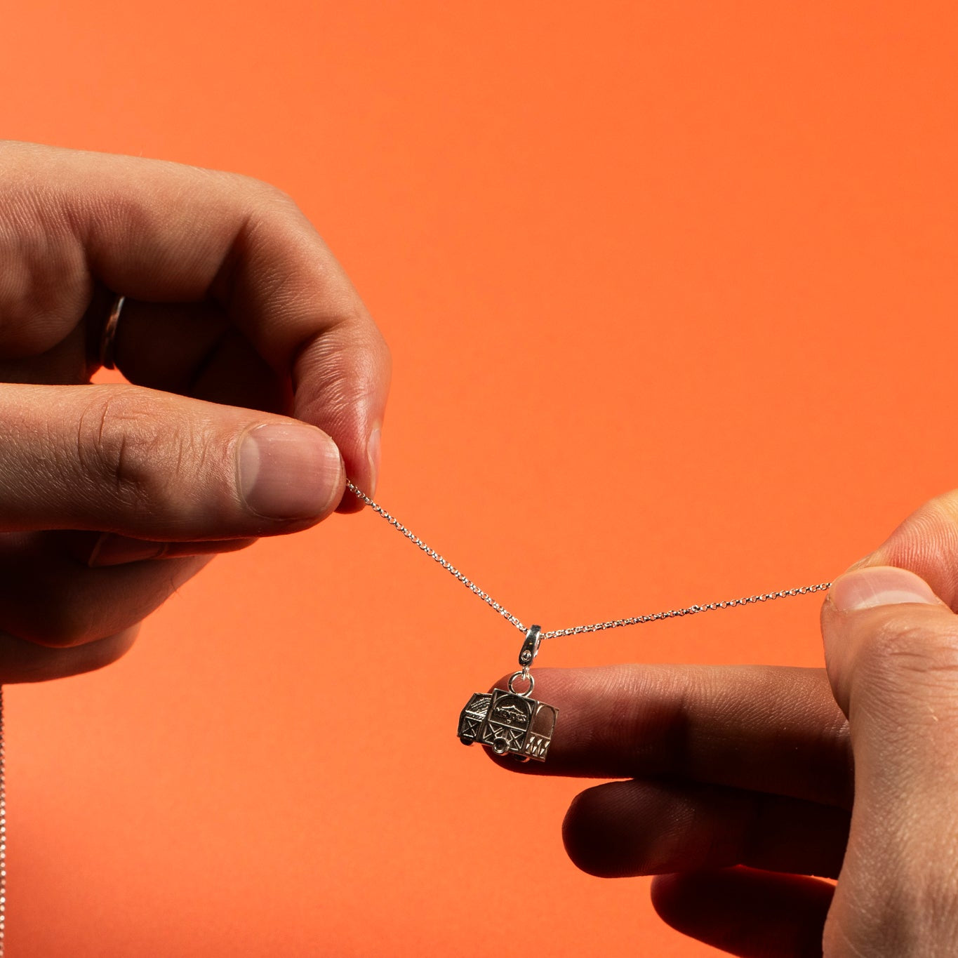 Person holding a necklace with a pendant against an orange background