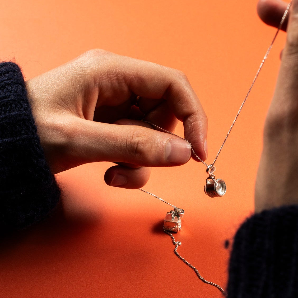 Close-up of hands holding a delicate necklace against an orange background