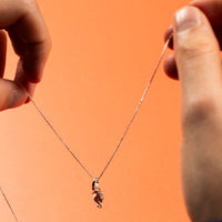Person holding a necklace with a small pendant against an orange background