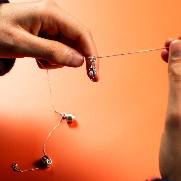 Two silver charms on a chain held by two hands against an orange background