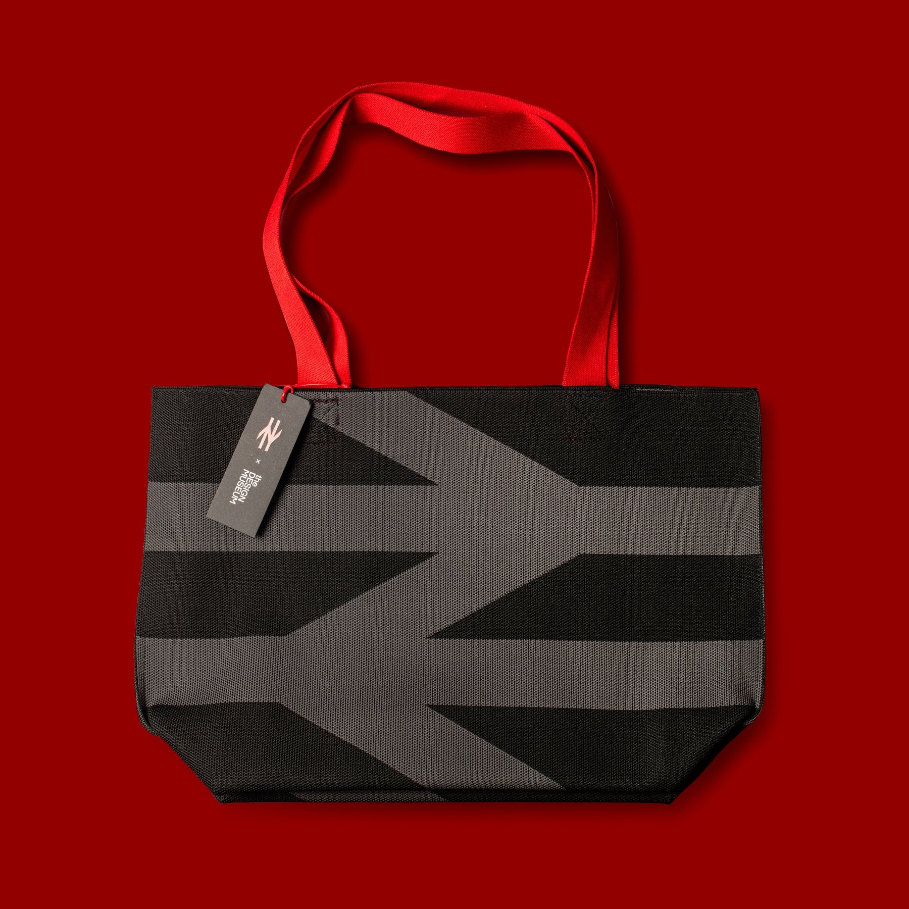 Black and gray striped tote bag with a red handle on a red background