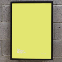 Yellow poster inside a black picture frame on a brick wall.