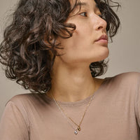 Woman with wavy hair wearing two heart necklaces against a neutral background