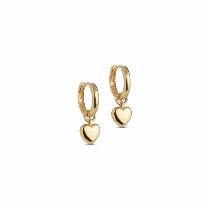 A pair of gold huggie hoop earrings with a small dangling heart charm, shown on a plain white background.